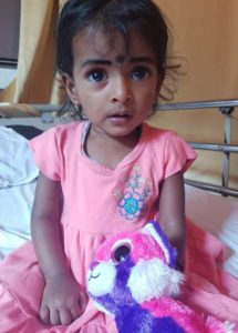 girl with big eyes sitting on hospital bed with toy