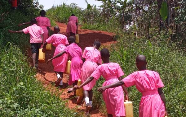 Ugandan girls in pink dresses carrying water cans on trail