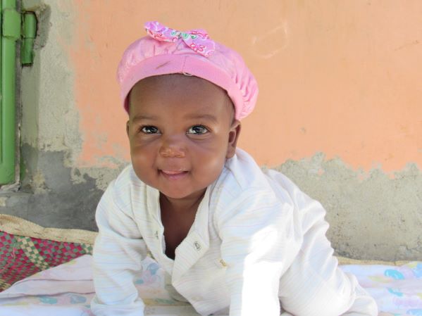 Ugandan baby girl in pink cap crawling towards camera