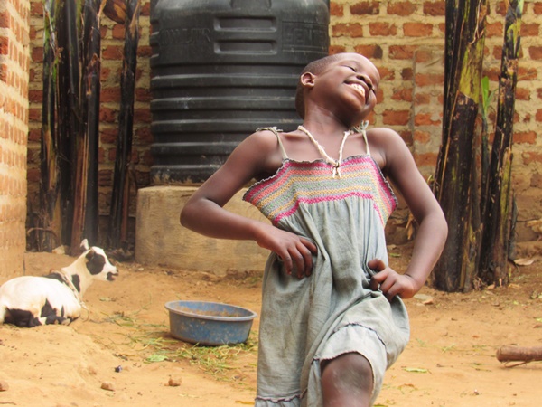 young girl smiling in Uganda with goat & water tank in background