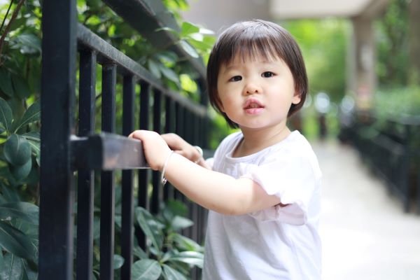 Toddler girl in white shirt standing by black gate