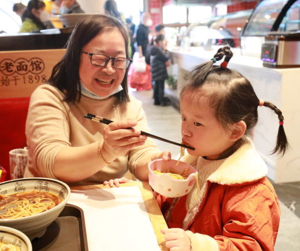 Woman feeding noodles to a girl with braids