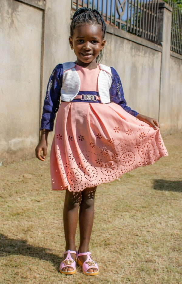 Ugandan girl in salmon colored dress in front of a wall waiting for heart surgery
