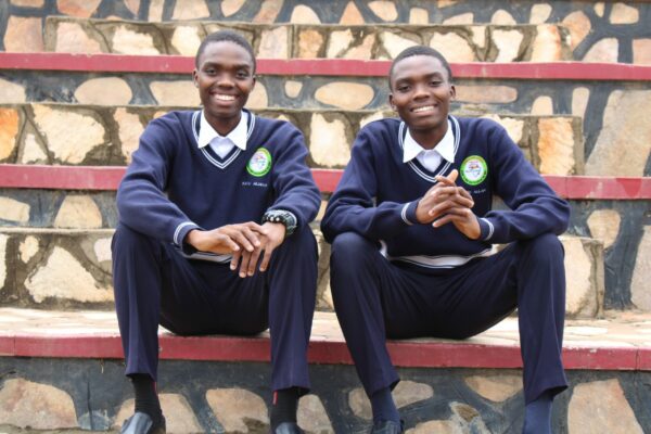 Twin brothers in school uniforms sitting on some steps in Uganda
