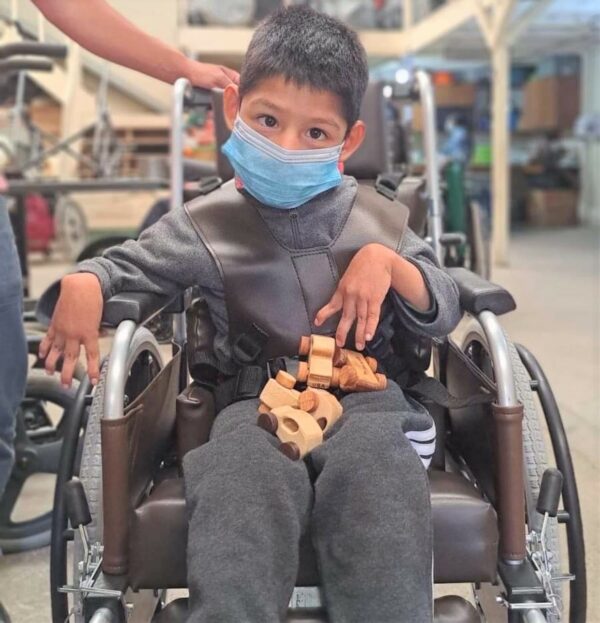 Boy wearing a mask in a wheelchair with wooden toys on his lap