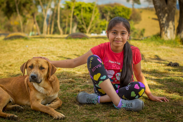 Girl in red shirt with hand on brown dog