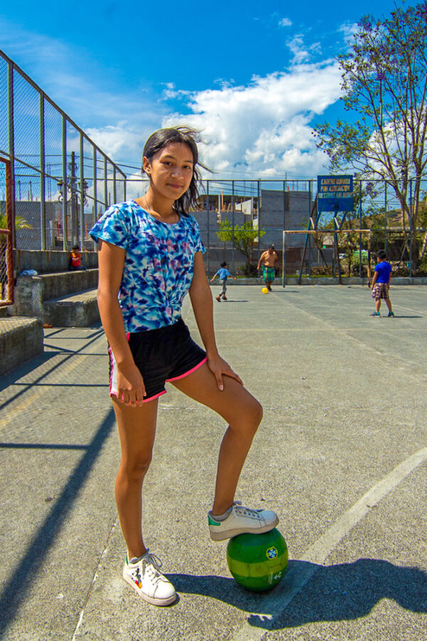 Girl on a Guatemalan playground has her foot on a green soccer ball