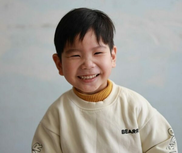 Chinese boy grinning in a whiteh sweatshirt with a mustard turtleneck