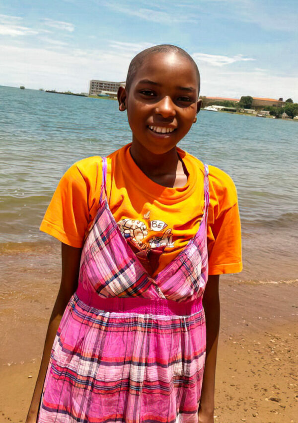 Girl in an orange t-shirt and pink plaid dress in front of a lake