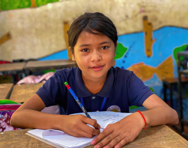 Girl in a blue Cambodian school uniform writing