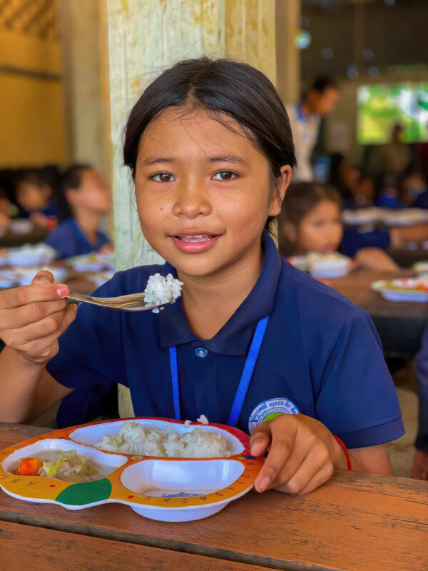 Girl in blue Cambodian school uniform eating rice