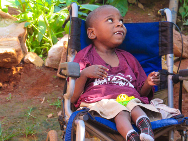 Small Ugandan boy sitting in a blue wheelchair outside