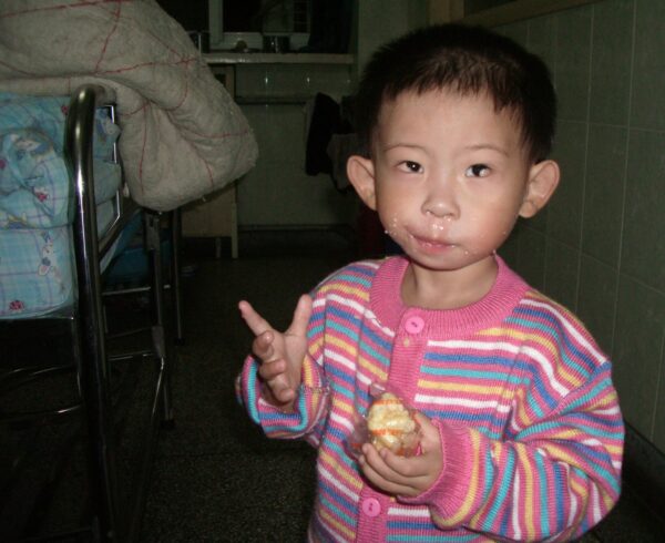 Little girl eating a rice cake snack in a striped sweater