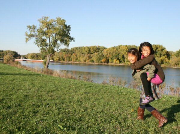 Two girls riding piggyback near a lake