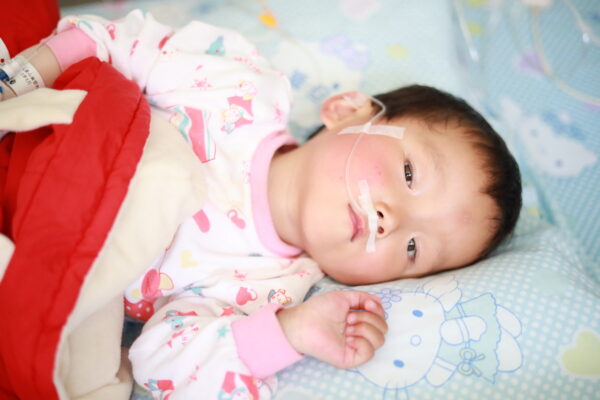 Toddler girl lying in hospital bed with red blanket