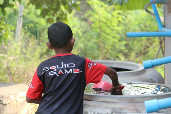 Boy in Squid Game shirt getting water from a well
