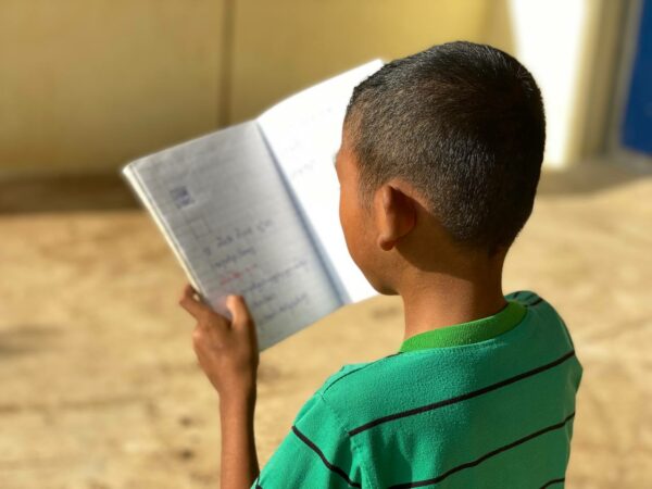 Boy in green striped shirt reading from a notebook