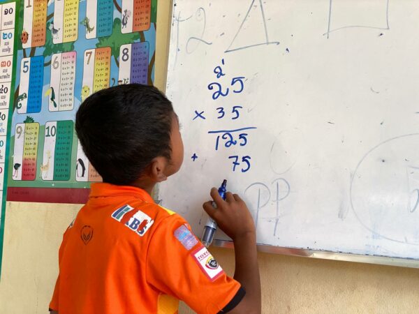 Boy in orange shirt writing on a whiteboard