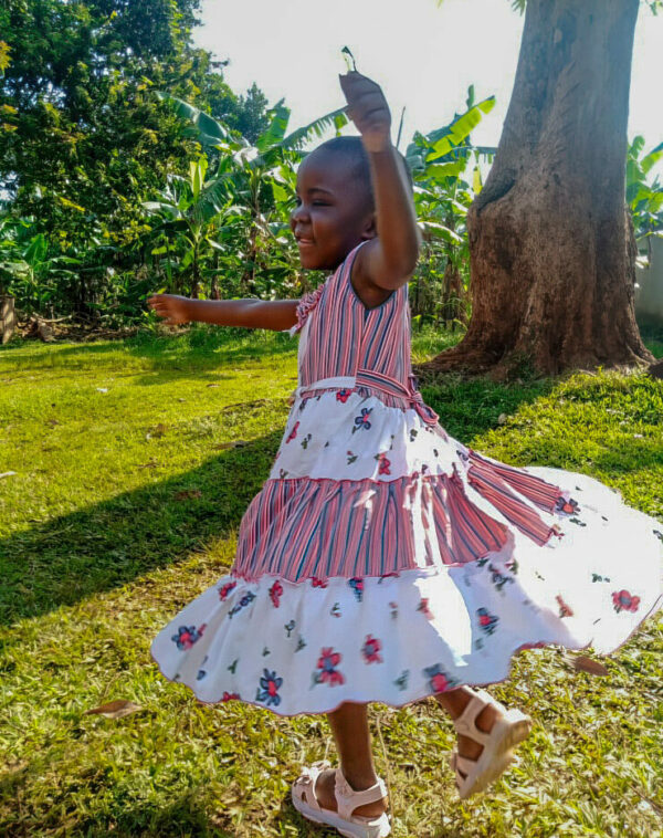 Young girl twirling in a dress with flowers and stripes outside near a tree