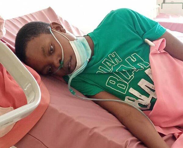 Young girl in a green T-shirt lying in a hospital bed with pink sheets