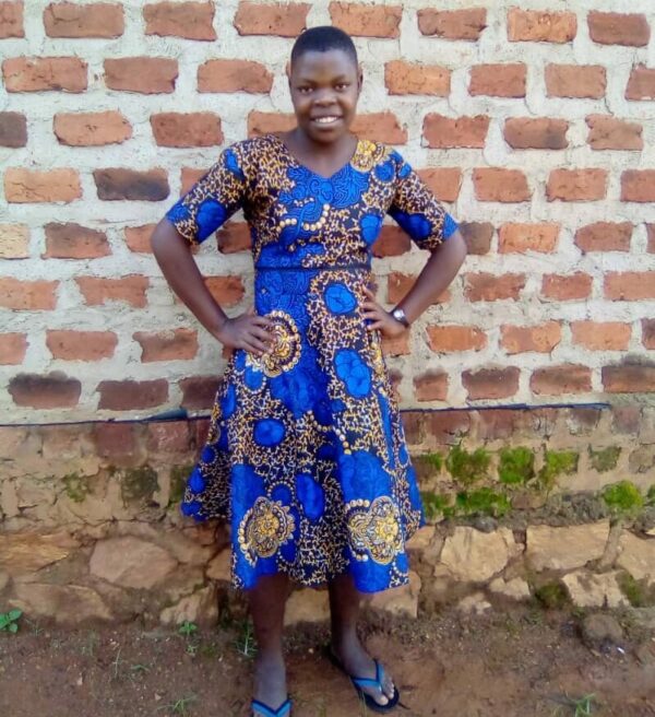 Young woman in Uganda wearing a bright blue dress in front of a brick wall