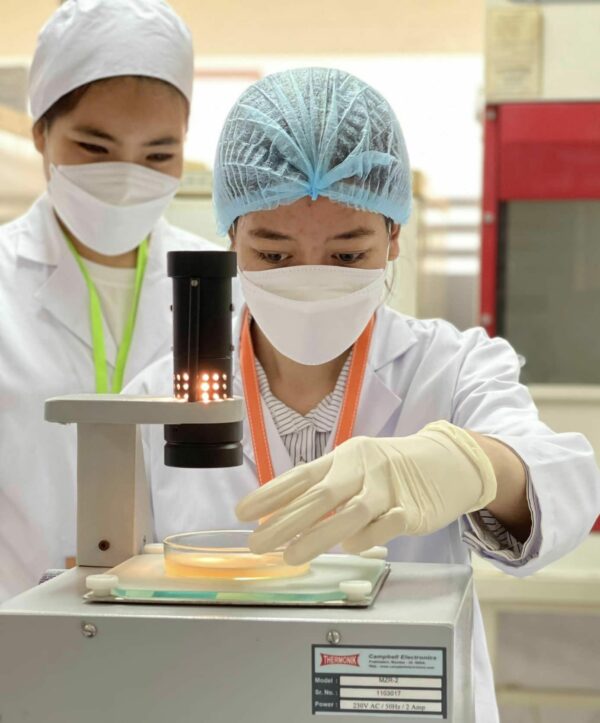 Two young women in lab coats and hats working in a lab