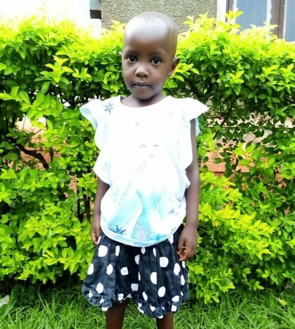 Little girl from Uganda stands in front of a green bush