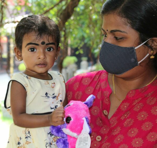 Little girl from India holding a stuffed animal in her mother's arms.