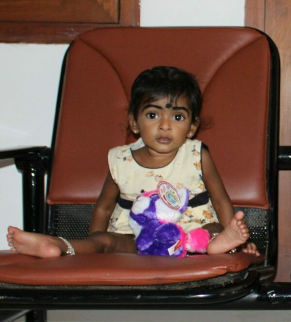 Tiny girl in India sitting on a large hospital chair with her stuffed animal