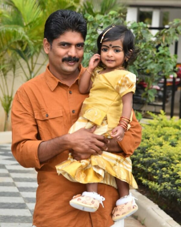 Father in an orange shirt holding his little daughter in a yellow dress in India