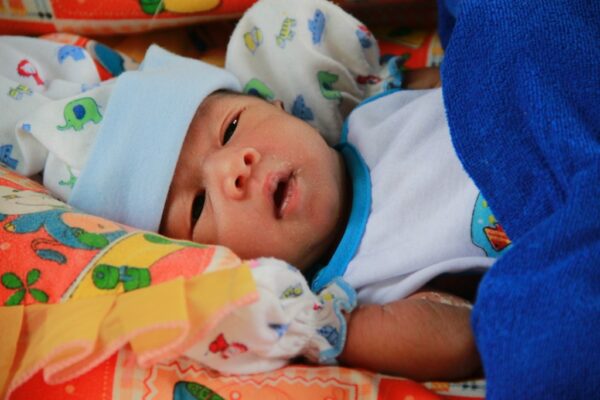 Cambodian newborn baby lying on his side in a blue cap