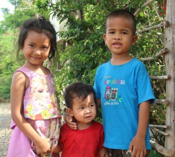 Three foster siblings in pink, red, and blue in Cambodia