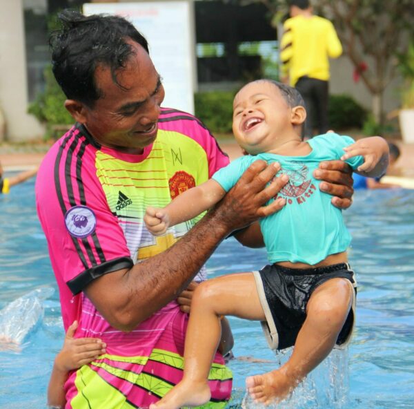 Dad plays with his son in a swimming pool in Cambodia as both laugh