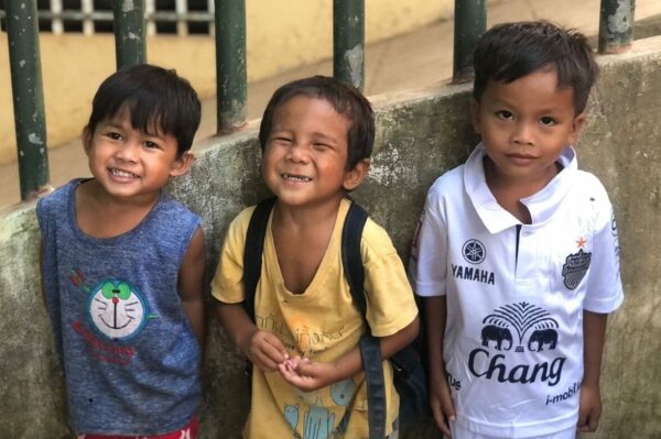 Three little boys smiling outside a school in Cambodia
