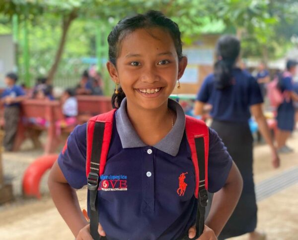Cambodian school girl wearing a blue school uniform and a red backpack