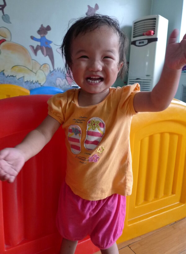 Toddler girl in orange and pink standing and laughing