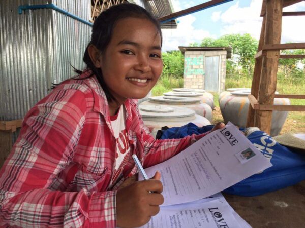 Teenage girl in red plaid shirt completing paperwork outdoors in Cambodia