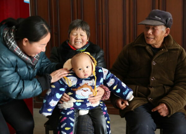 Chinese grandparents and mom surround a baby boy in a quilted snowsuit