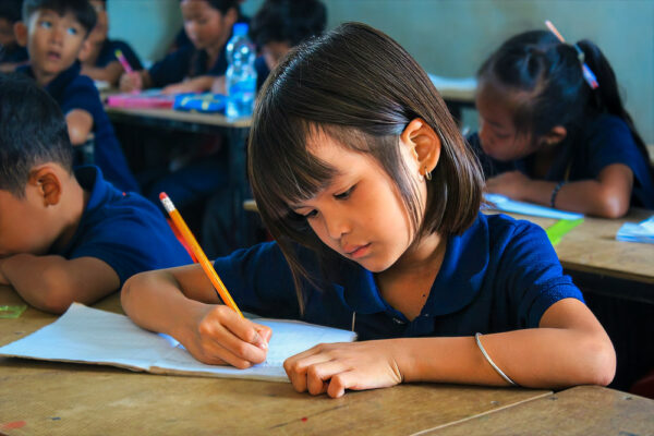 Girl in blue school uniform writes with a pencil at school.