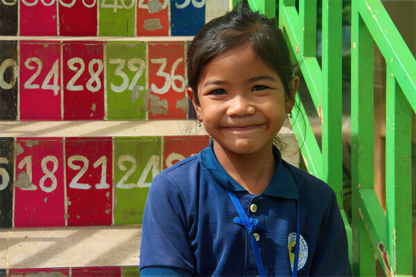 Girl in blue school uniform sits on steps of LWB's Believe In Me Cambodia school