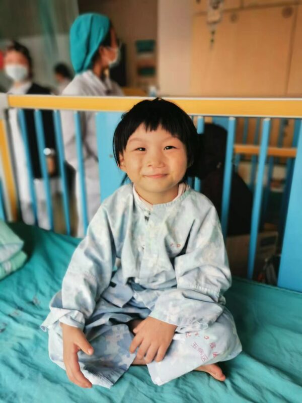 Little girl in blue sits in a hospital bed