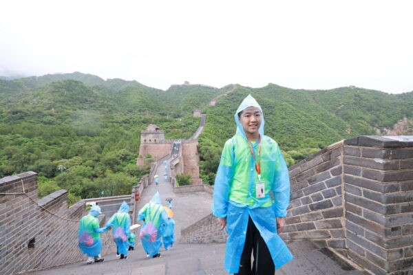 Teen boy in a blue raincoat stands on the Great Wall of China