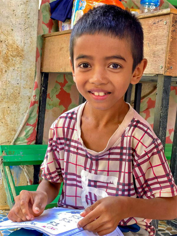 Little boy in a plaid shirt reads a book in Khmer