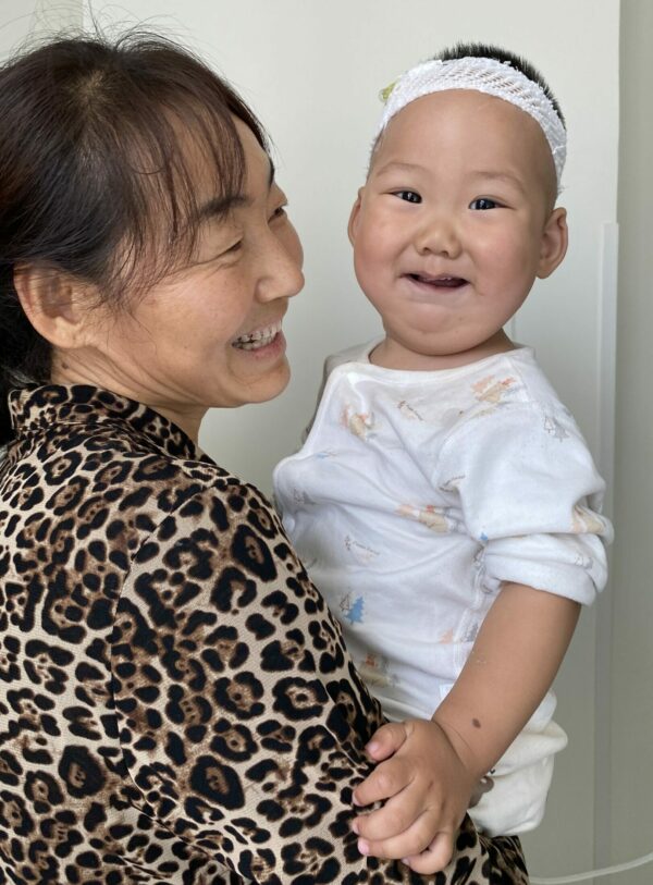 Baby in white pajamas being held by smiling grandma