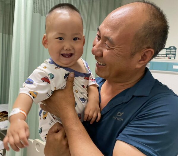 Laughing baby being held by his smiling grandfather in hospital