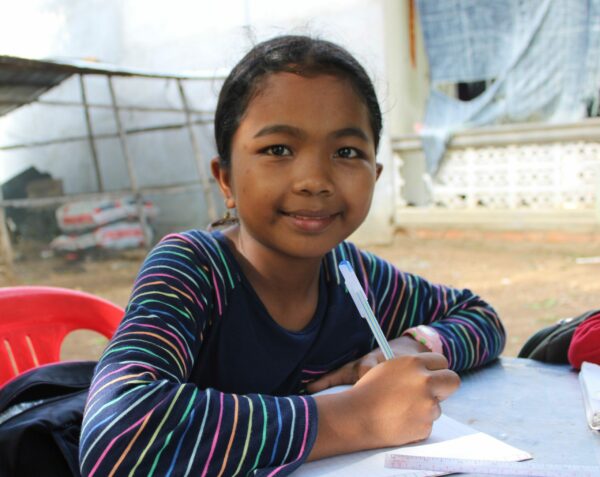 Girl holding a pen does homework outside in Cambodia