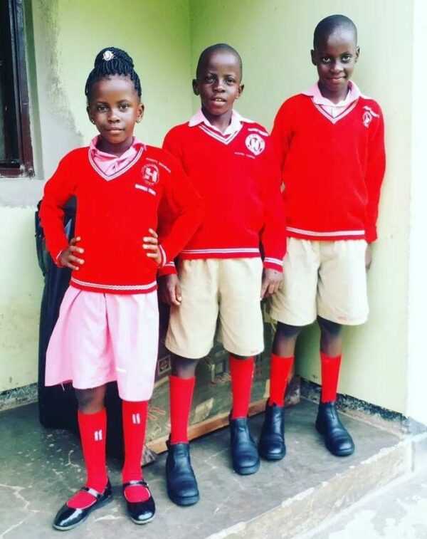 Three children standing in a row wearing Ugandan school uniforms