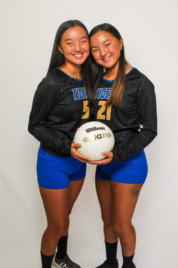 Twin girls in matching volleyball uniforms hold a volleyball