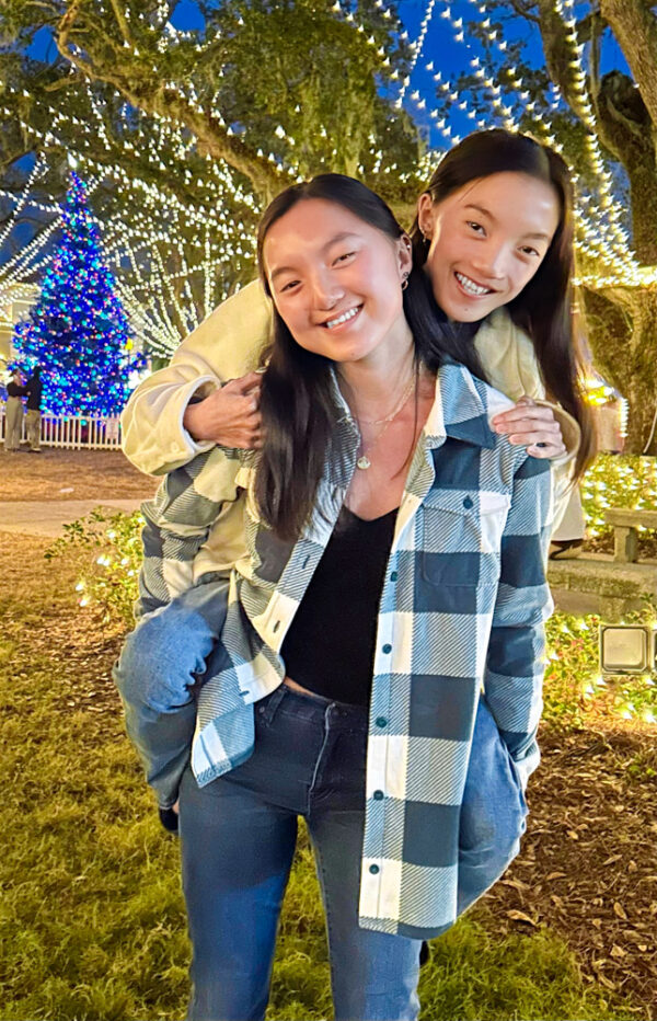 Teen twin girls stand in front of Christmas lights