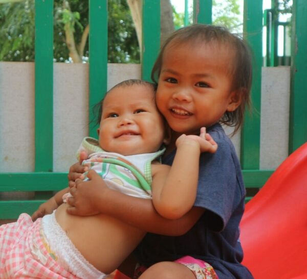 A toddler girls hugs her baby sister